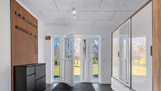 A modern reception area with a black console, wooden panel wall, and a view of the outdoors through glass doors.
