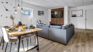 A modern living space with a dining area, a grey sofa, a flat-screen TV, and a wooden ceiling.