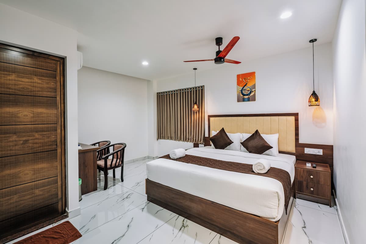 A modern hotel room with a large bed, a desk, a chair, a ceiling fan, and a nightstand.