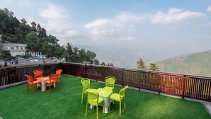 A rooftop terrace with green artificial grass, orange and yellow chairs, and a view of a mountainous landscape. - Mountain Villa Mussoorie  (Mussoorie)