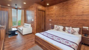 A modern bedroom with a wooden ceiling, a bed with floral bedding, a white sofa, and a view of the outdoors. - Mountain Villa Mussoorie  (Mussoorie)