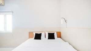 A hotel room with a bed, two black and white pillows, a wooden headboard, a white wall, and a window. - Hotel O Bogor near Taman Safari formerly Hotel Rudian 2 (Cisarua)