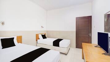 A hotel room with two beds, a wooden desk, a television, and a door.