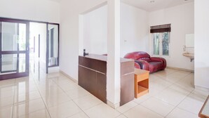 A spacious room with a large sliding glass door leading to an outdoor area, a wooden reception desk, a red leather sofa, and a sink in the corner. - Hotel O Bogor near Taman Safari formerly Hotel Rudian 2 (Cisarua)
