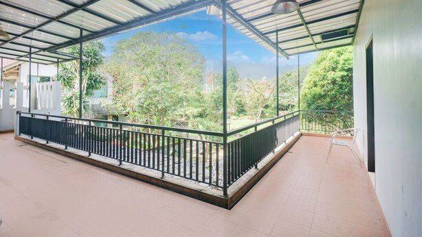 A covered balcony with a metal railing, a tiled floor, and a view of greenery and buildings. - Hotel O Bogor near Taman Safari formerly Hotel Rudian 2 (Cisarua)