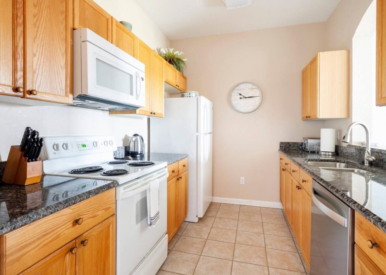 A kitchen with wooden cabinets, a white stove, a microwave, a refrigerator, and a clock on the wall.