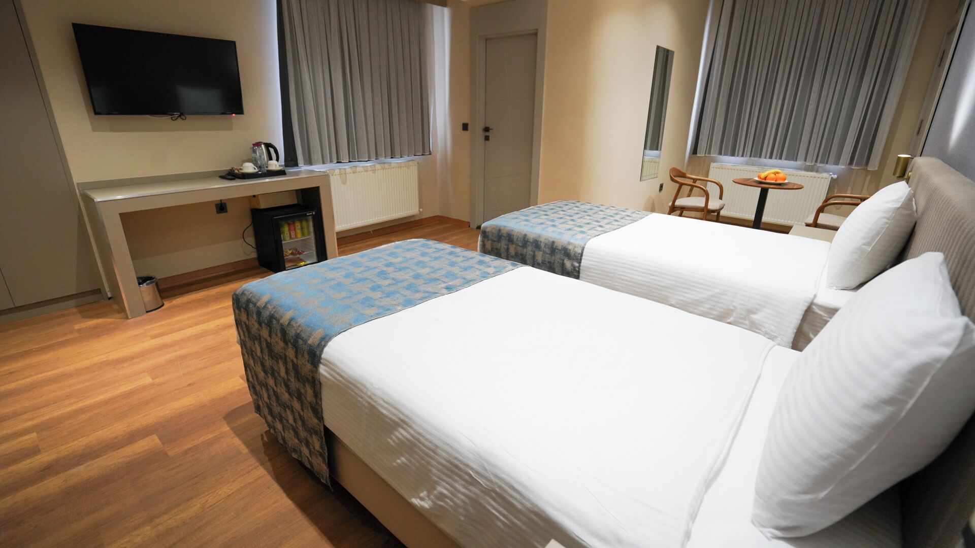 Habitación de hotel con dos camas, un escritorio, televisión y un refrigerador pequeño.