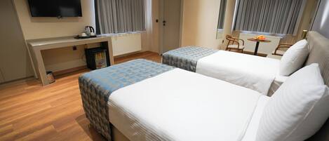 Habitación de hotel con dos camas, un escritorio, televisión y un refrigerador pequeño.