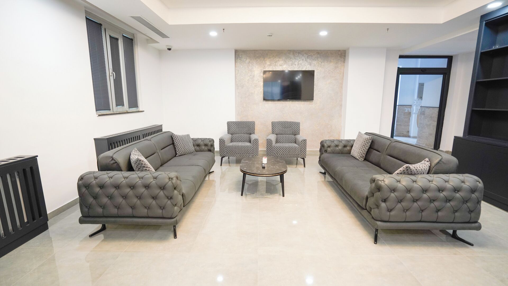 Uma sala de estar moderna com dois sofás cinzas, uma mesa de centro e poltronas estampadas.