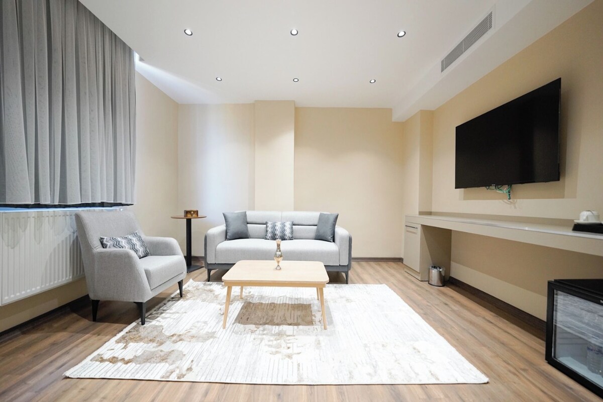 A modern living room with a grey sofa, a small armchair, a coffee table, and a flat-screen TV mounted on the wall.