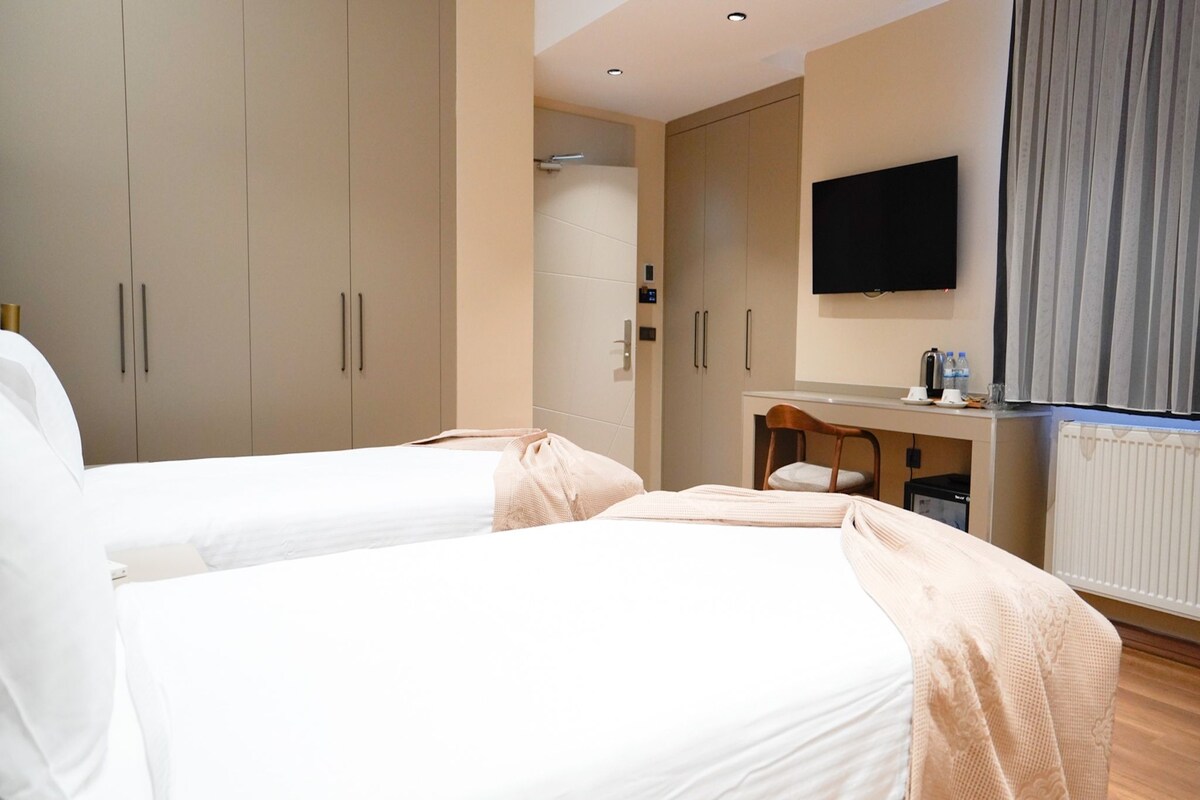 A hotel room with two beds, a TV, a desk with a chair, and a radiator.