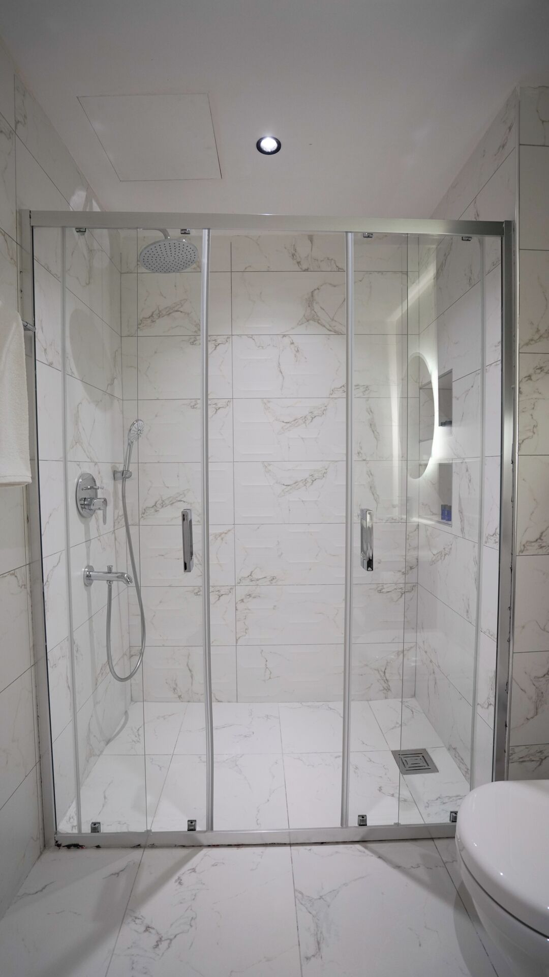 Un baño moderno con cabina de ducha de vidrio, baldosas de mármol y un inodoro.
