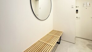 Ένα μινιμαλιστικό μπάνιο με ένα ξύλινο παγκάκι, έναν στρογγυλό καθρέφτη και μια πόρτα με πίνακα ελέγχου.