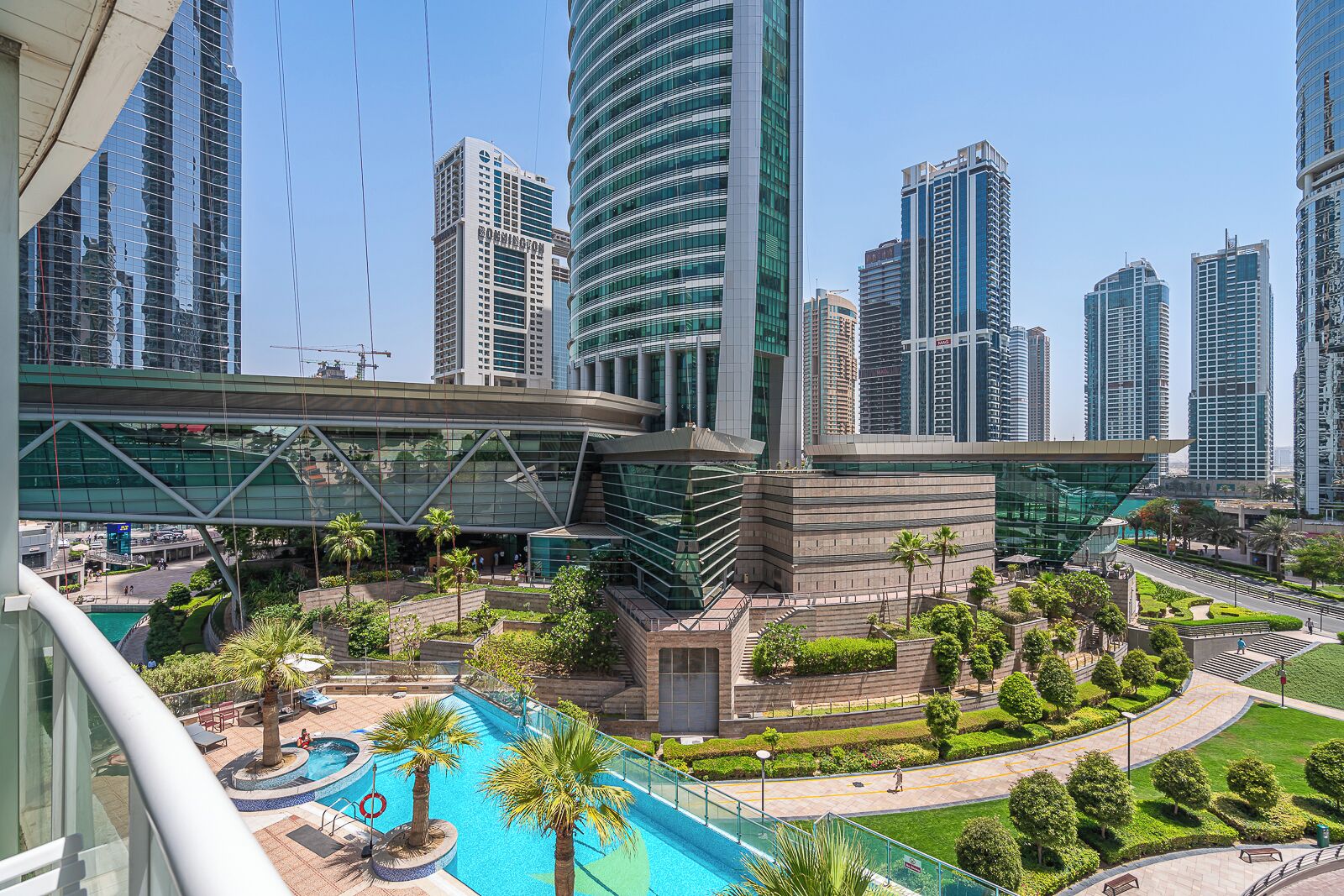 A modern urban area with high-rise buildings, a central plaza with a pool, and palm trees.