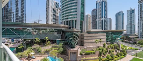 A modern urban area with high-rise buildings, a central plaza with a pool, and palm trees.