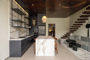 A modern kitchen with marble countertops, a central island, and built-in shelves. - Rocca Bella Loft 4 by Alfred in Bali (Canggu)