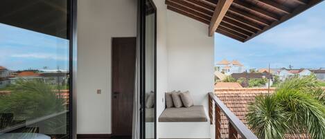 A balcony with a wooden ceiling, a glass door leading to a room, and a view of houses in the background.
