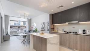 A modern kitchen with a marble countertop, dark cabinets, and a city view.