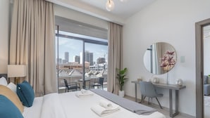 A modern hotel room with a large bed, a desk, and a view of the cityscape.