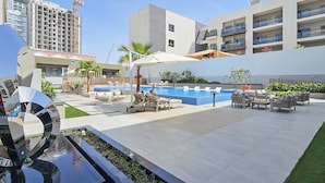 A modern outdoor pool area with lounge chairs, a decorative sculpture, and a view of surrounding buildings.