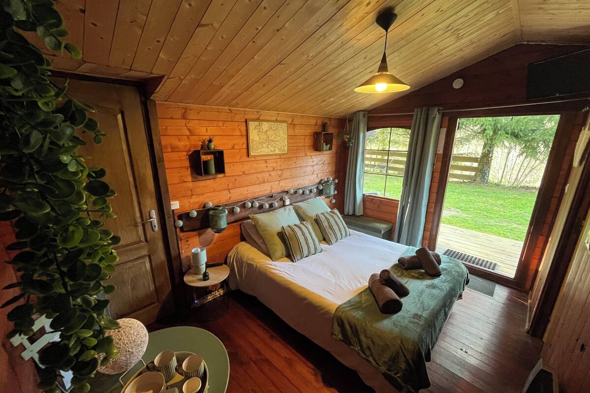 A wooden cabin bedroom with a bed, bedside table, and a view of the outdoors.