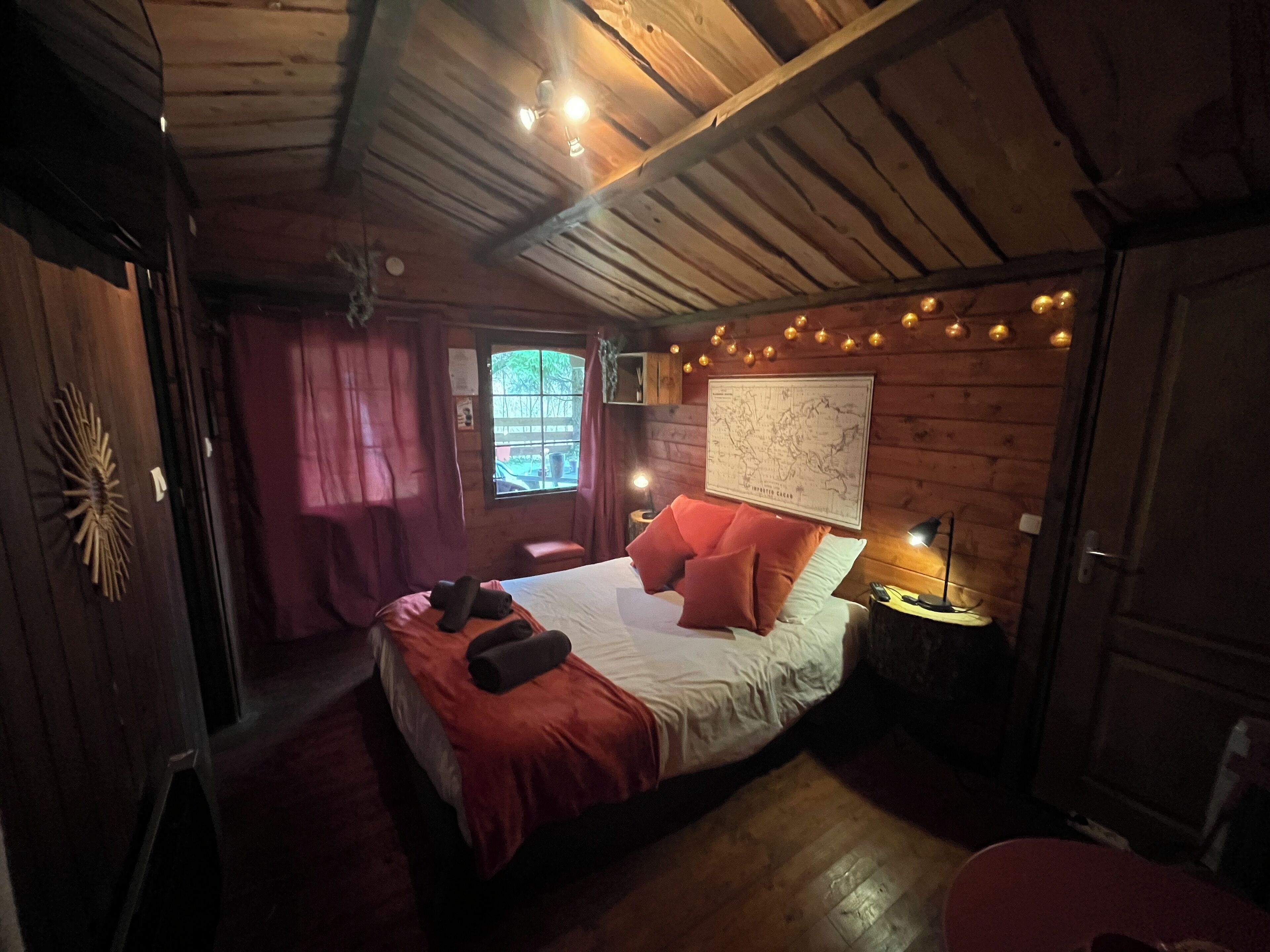 A cozy wooden cabin bedroom with a bed, a map on the wall, and string lights.