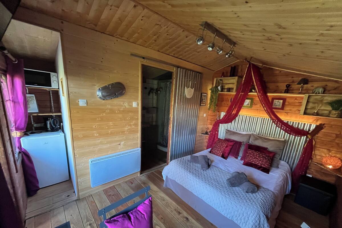 A cozy wooden cabin bedroom with a bed, a small desk, and a bathroom.