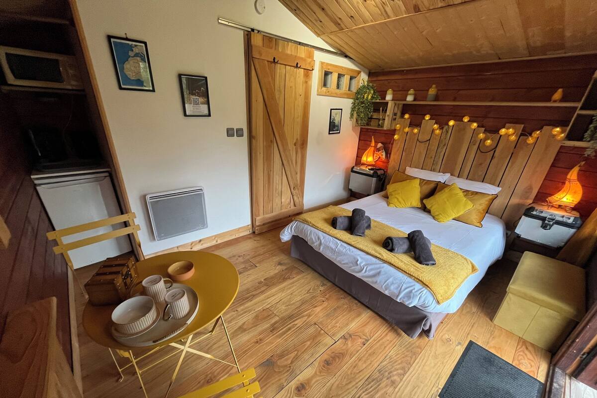 A cozy room with a bed, bedside lamps, a small table with bowls, and a chair.