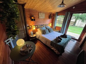 A cozy wooden room with a bed, bedside lamps, a table with cups, and a view of the outdoors. - LE MALOYA (Lacaune)