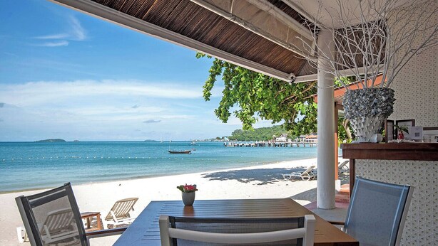 A beachside patio with a table and chairs, overlooking a sandy beach and the ocean. - Aqua Beads Samed (Rayong)