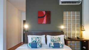 A hotel room with a large bed, a headboard, a wall-mounted air conditioner, a decorative painting, a wall-mounted light fixture, and a nightstand with a lamp. - Aqua Beads Samed (Rayong)