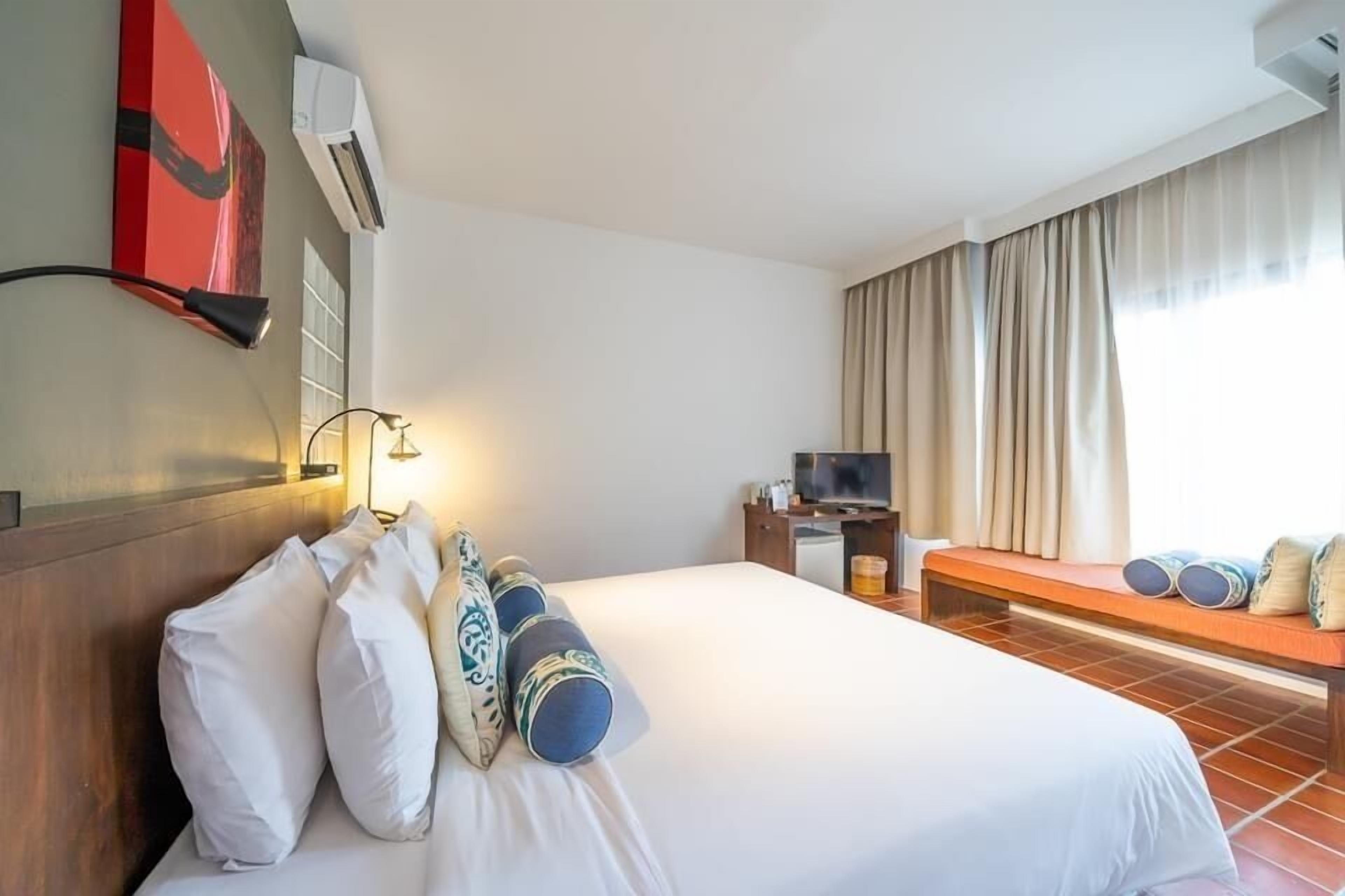 Una habitación de hotel con una cama grande, televisión, escritorio y ventana con cortinas.
