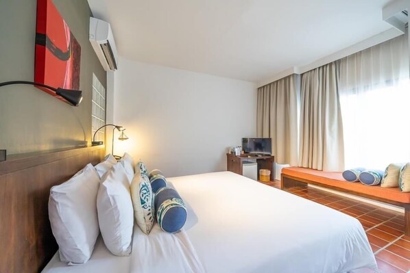 A hotel room with a large bed, a TV, a desk, and a window with curtains. - Aqua Beads Samed (Rayong)