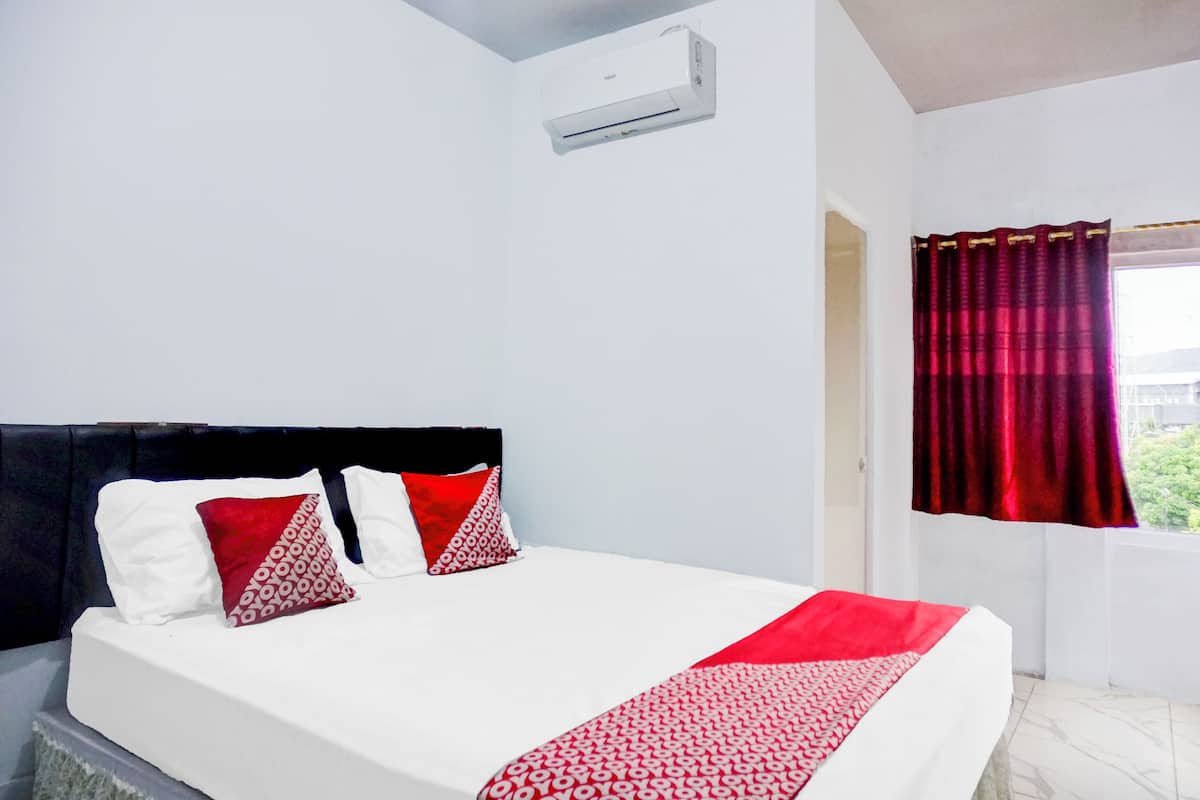 A hotel room with a bed, a window with red curtains, and an air conditioning unit on the wall.