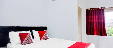 A hotel room with a bed, a window with red curtains, and an air conditioning unit on the wall.