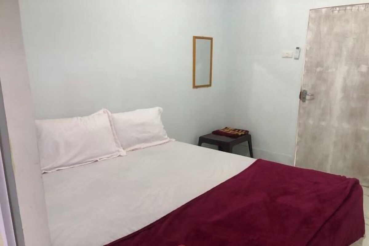 A bedroom with a bed, a small table, a mirror, and a door.