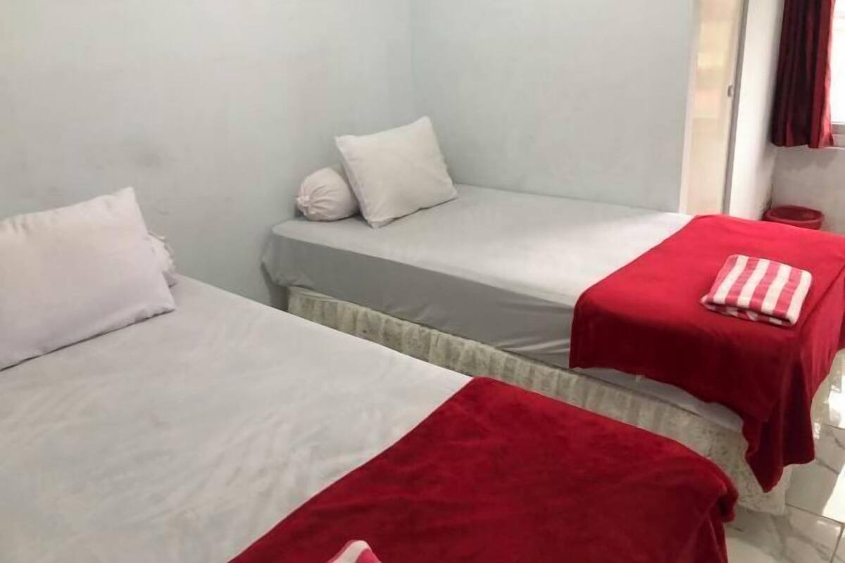 A room with two beds, each with a red blanket and pillow.