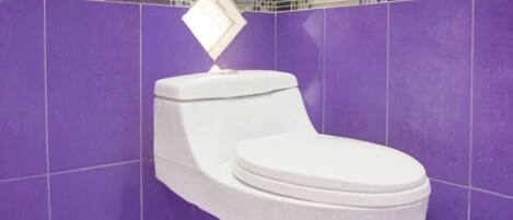 Un baño con azulejos morados, un inodoro blanco y azulejos decorativos en la pared.