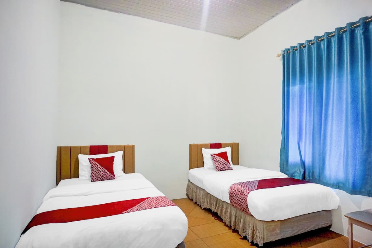 A hotel room with two beds, each with white bedding and red accents, a wooden headboard, and a blue curtain on the window.