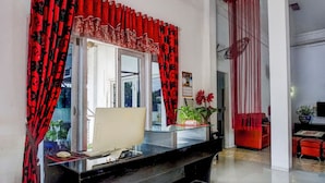 A room with a black desk, a computer, and a glass display case. There is a red curtain with a floral pattern, a white wall, and a red sofa in the background. - Hotel O Banda Aceh near Masjid Raya Baiturrahman formerly Wisma Tsacita (Banda Aceh)