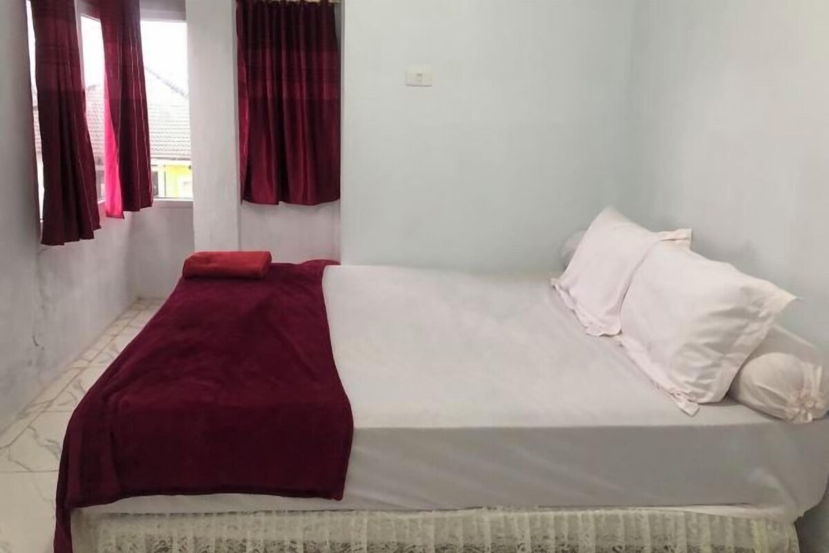 A single bed with a white mattress and red blanket, white pillows, and red curtains.