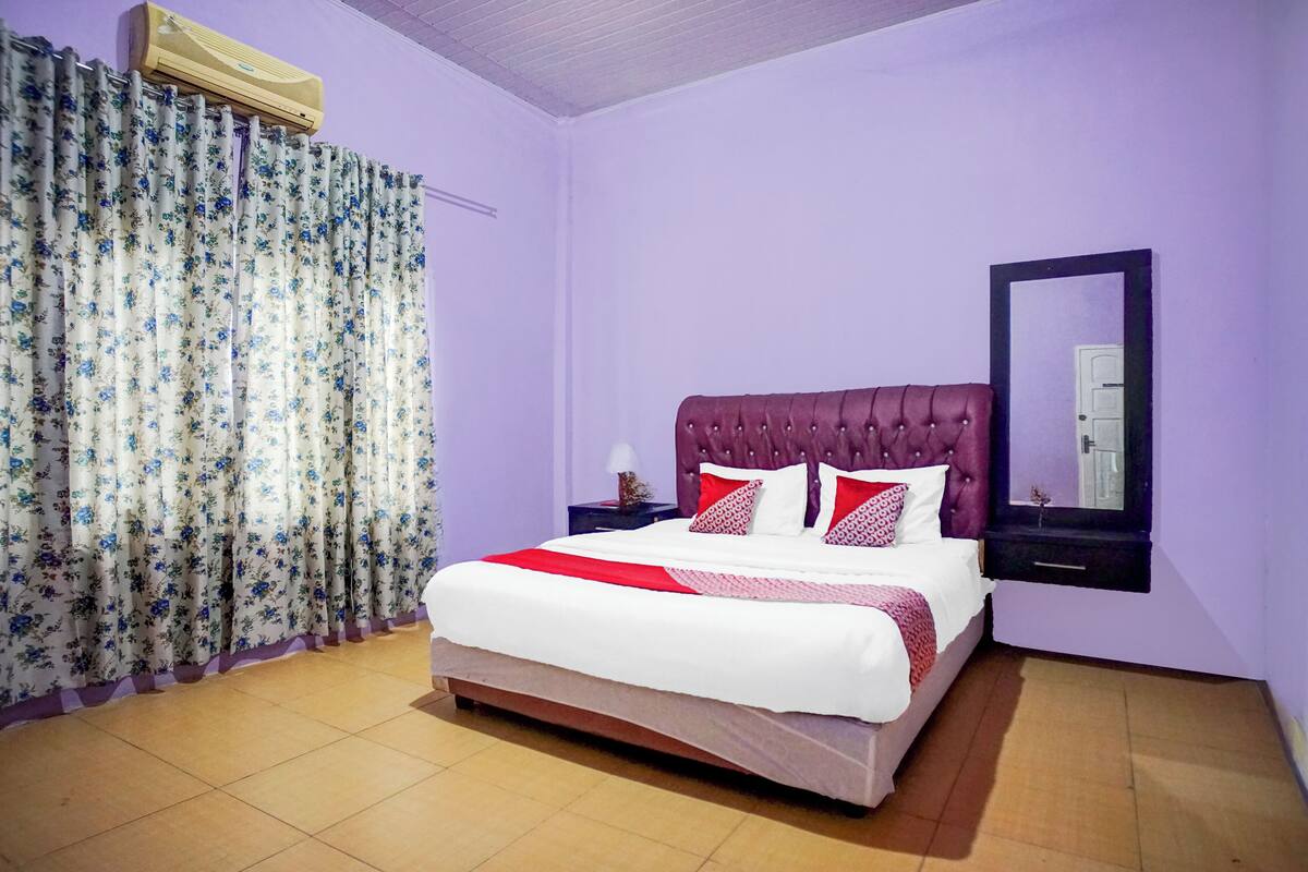A bedroom with a bed, curtains, a nightstand, a mirror, and an air conditioning unit.