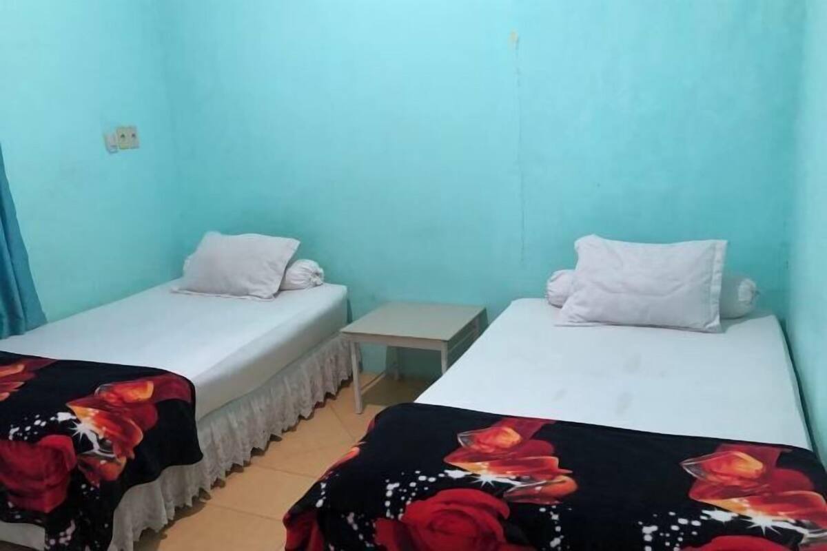 A room with two single beds, each with a white pillow and a floral bedspread. There is a small white table between the beds.