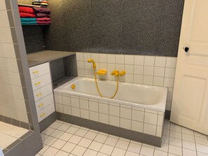 Bathroom features a white bathtub with a showerhead and hose, and a shelf for towels.