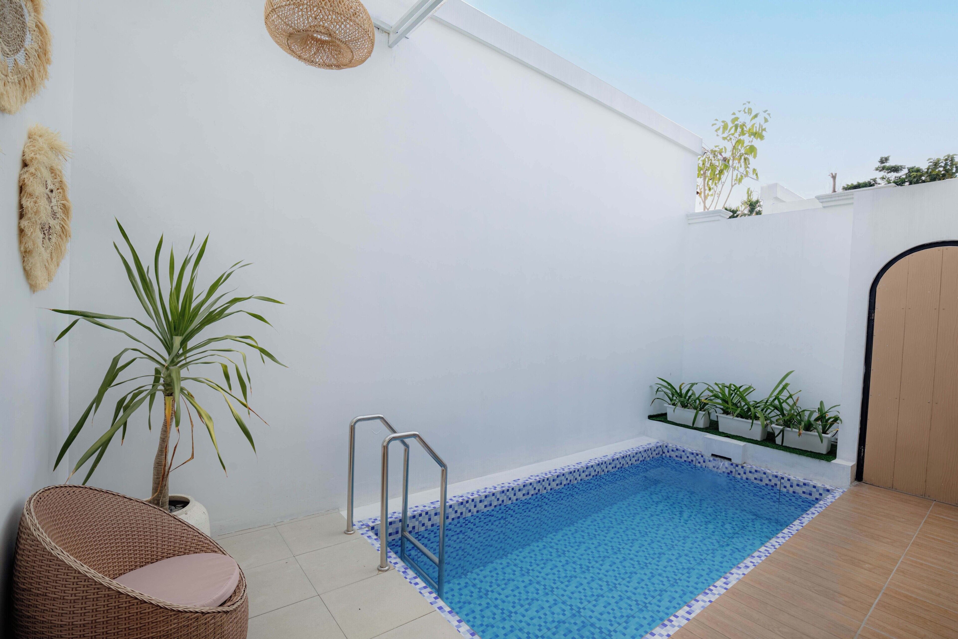 A small indoor pool with a tiled edge, a wicker chair, and potted plants.
