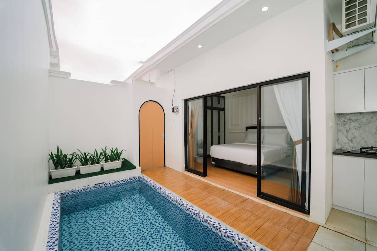 Une chambre d’hôtel moderne dotée d’une petite piscine, d’une porte-fenêtre coulissante donnant sur un balcon et d’un coin cuisine.