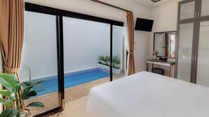 Ein Hotelzimmer mit einem großen Bett, einem Schreibtisch mit Stuhl, einem an der Wand montierten Fernseher und einer Schiebeglastür, die zu einem Poolbereich führt.