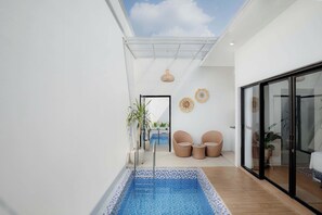 A modern interior with a pool, wicker furniture, and a glass door leading to a balcony. - Marina Villa 1 (Ngaglik)