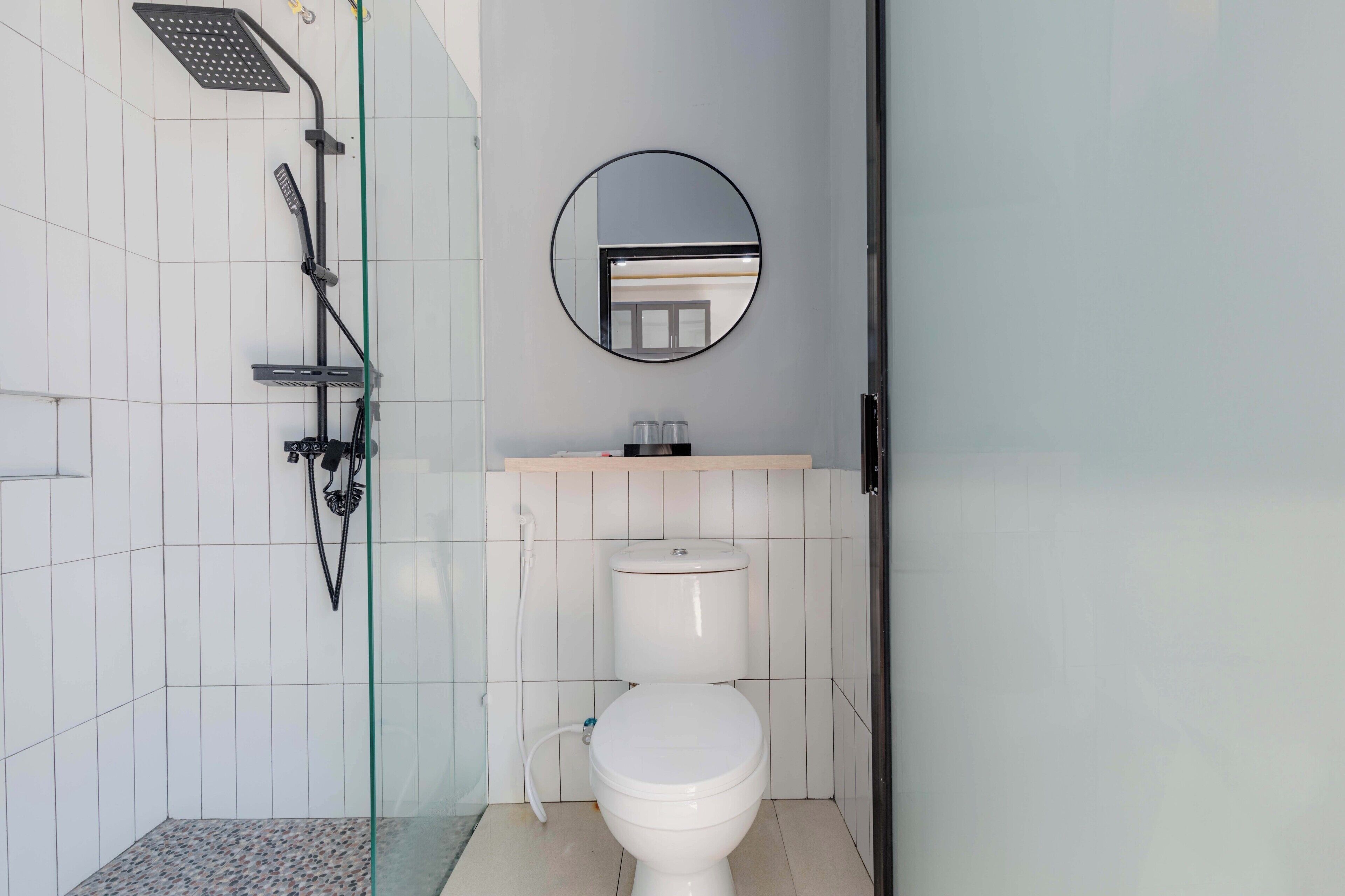 Un baño con inodoro, ducha con puerta de cristal, espejo y lavamanos con encimera.