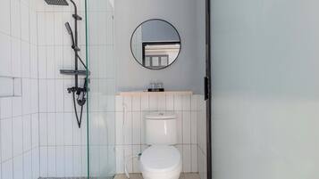 Un baño con inodoro, ducha con puerta de cristal, espejo y lavamanos con encimera.